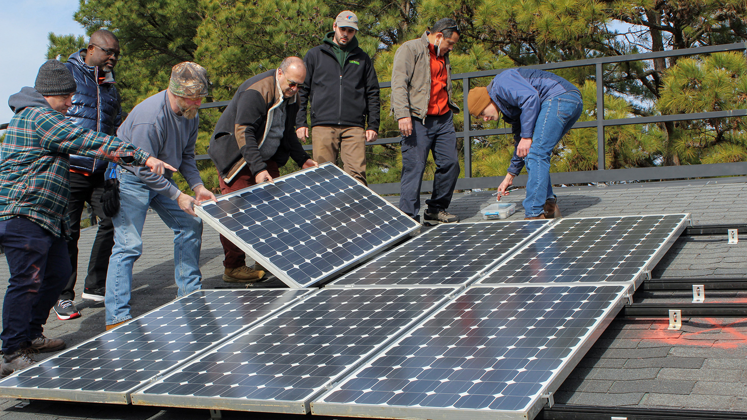 A group of installers lay a rectangular solar panel into a larger array.