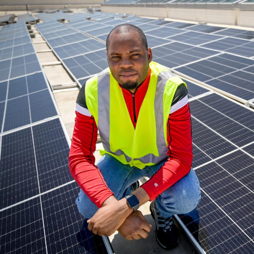 Raheem Ariwoola sits by solar panels on top of Fitts-Woolard Hall wearing yellow safety vest.